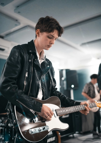 Dreng iført læderjakker står og spiller på en sort elektrisk guitar af modellen Fender Telecaster