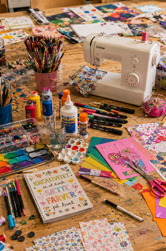 Et bord med symaskine, stofrester, gelelys og malilng